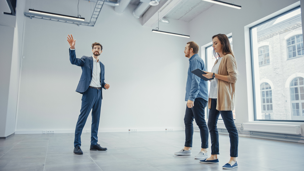 Real Estate Agent Showing a New Empty Office Space to Young Male and Female Hipsters. Entrepreneurs Meet the Broker with a Tablet and Discuss the Facility They Wish to Purchase or Ren