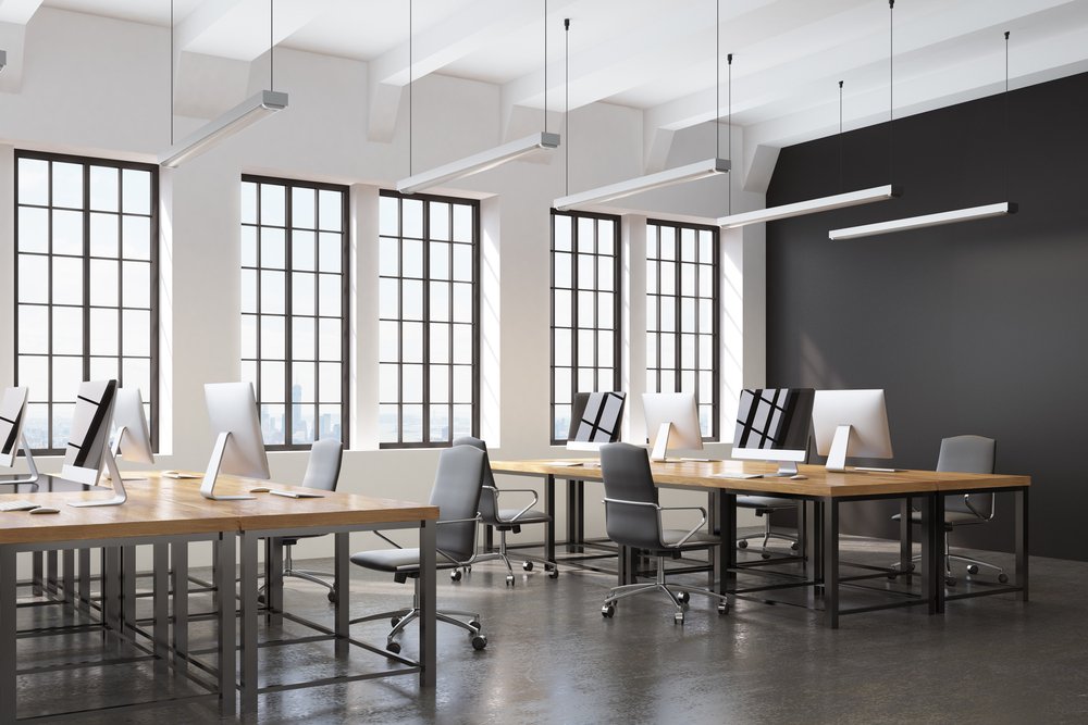 Side view of an open space office with a black wall, many tables with computers on them and a concrete floor. 3d rendering